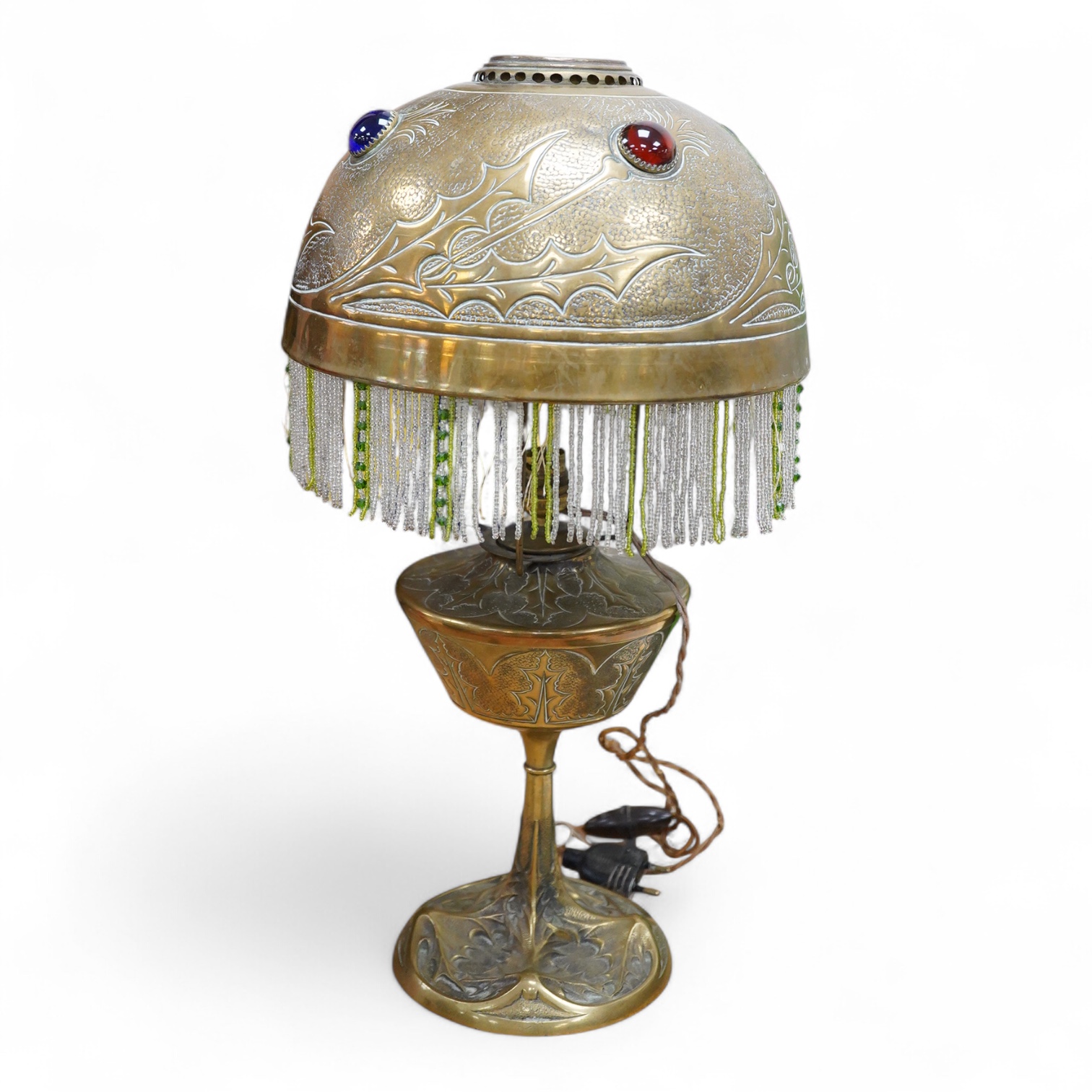 After Georges Leleu, an Art Nouveau brass oil lamp converted to electricity, with glass cabochon roundels and beaded fringing, 50cm high